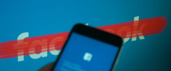 Celular con la aplicaciÃ³n de Facebook, delante de un logo de Facebook tachado.