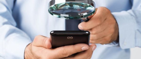 Hombre sosteniendo una lupa sobre un celular.