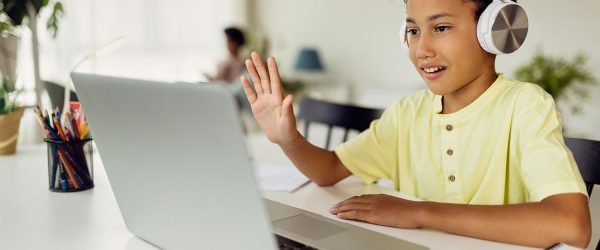 Smiling black boy making video call over laptop and waving while e-learning at home.