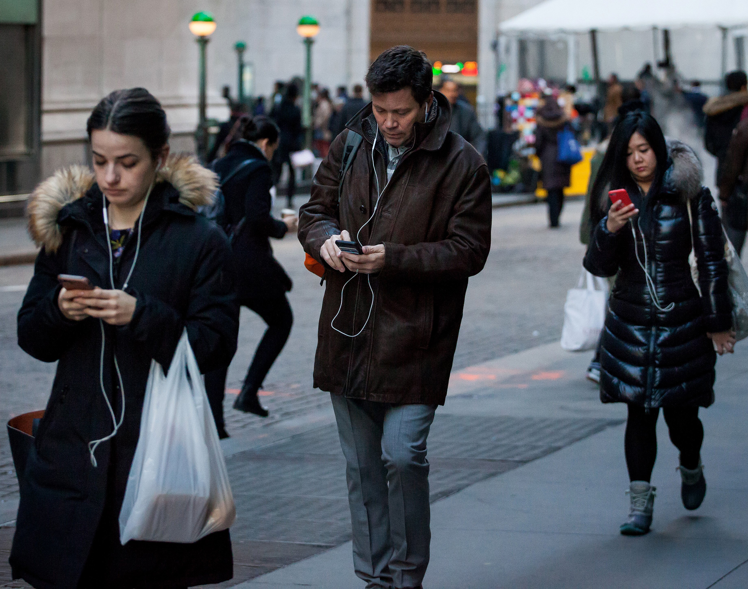 Pedestrians walk along Wall Street while looking at their smartphone devices in front of the New York Stock Exchange (NYSE) in New York, U.S., on Monday, March 20, 2017. U.S. stocks fluctuated about 1 percent below all-time highs, while oil fell toward $48 a barrel. Photographer: Michael Nagle/Bloomberg via Getty Images